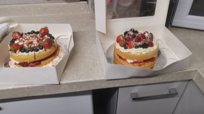 Two sponge cakes topped with cream and fresh fruit, boxed and ready to take home