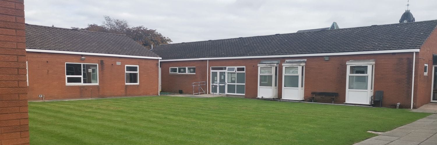 The single storey red brick Madrasah Salaam building, with a lawn and a low hedge along the pavement