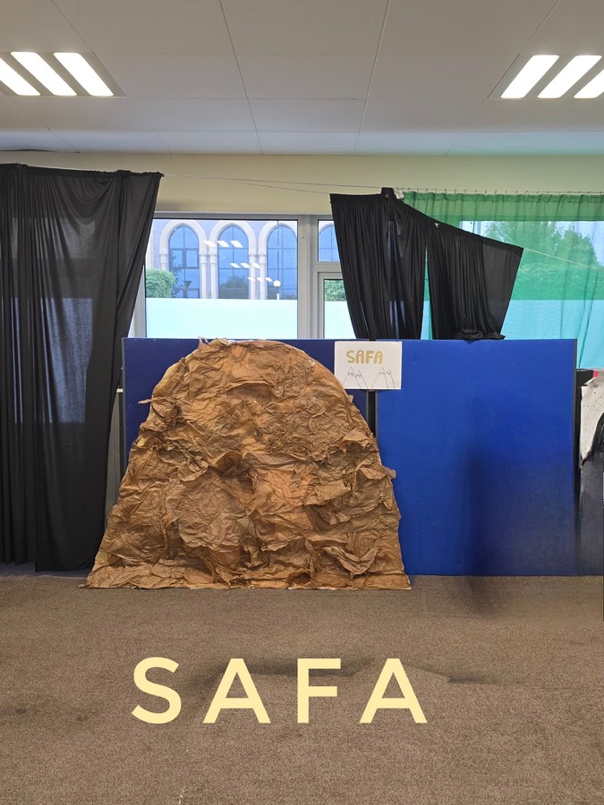 A large hand built rocky hill in a room hung with dark drapes, standing on brown floor covering