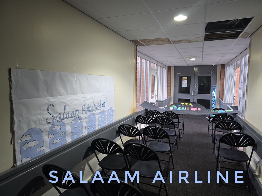 A classroom laid out in rows of chairs as an aircraft cabin, with a Salaam Airline banner across the far wall