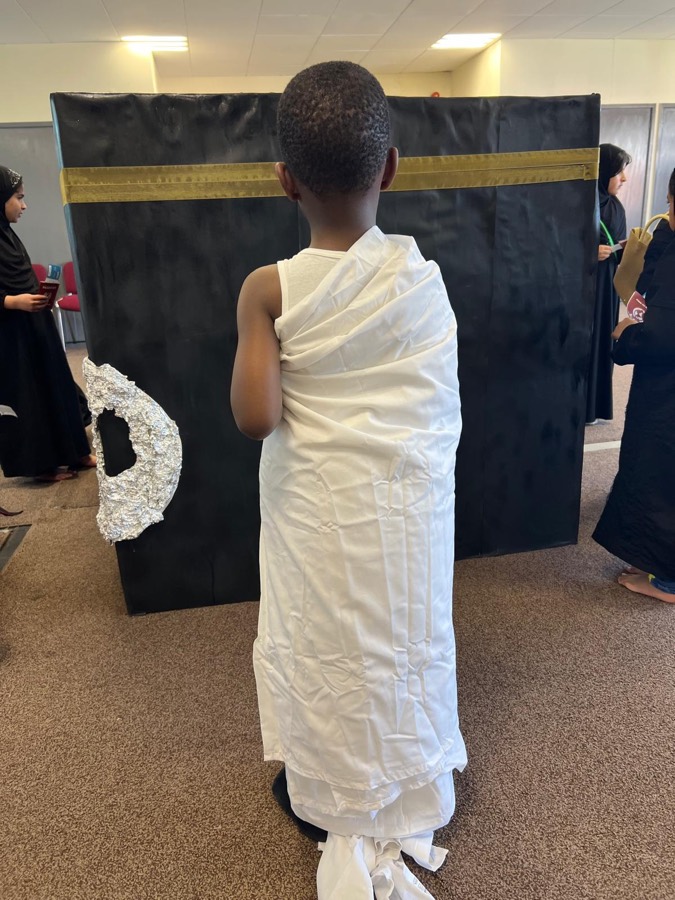 A child seen from behind, wearing ihram, standing at a doorway hung with dark fabric